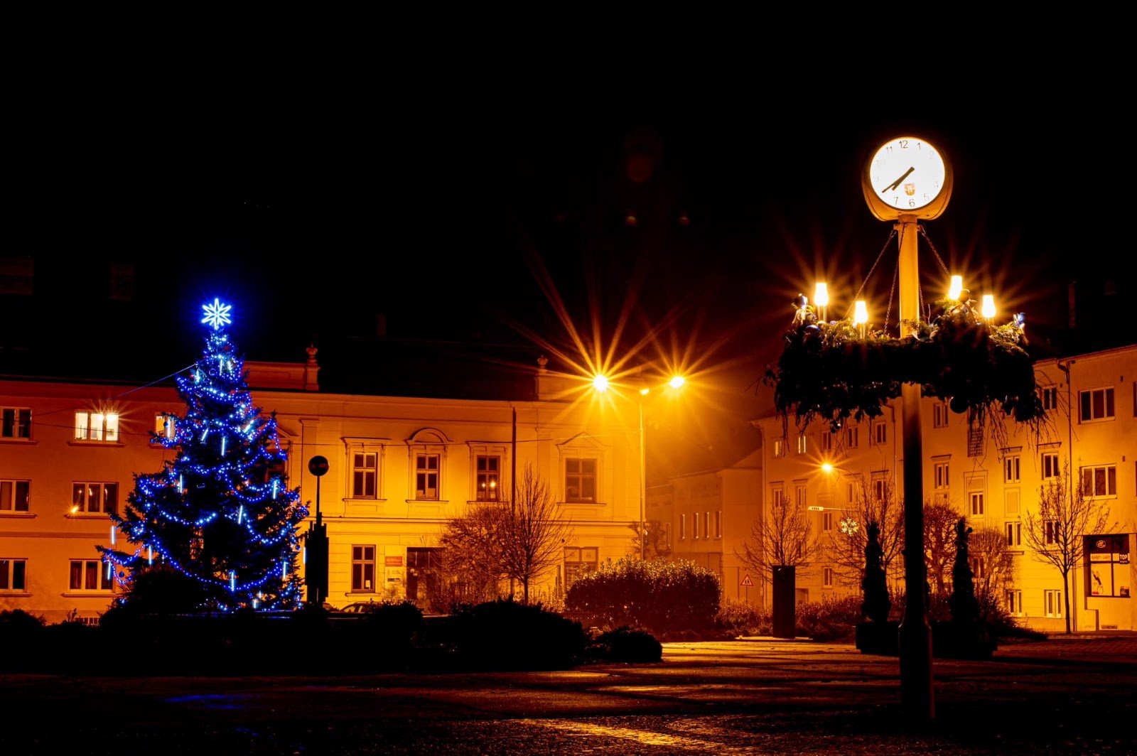 Árvore de Natal iluminada e iluminação pública numa praça municipal à noite.